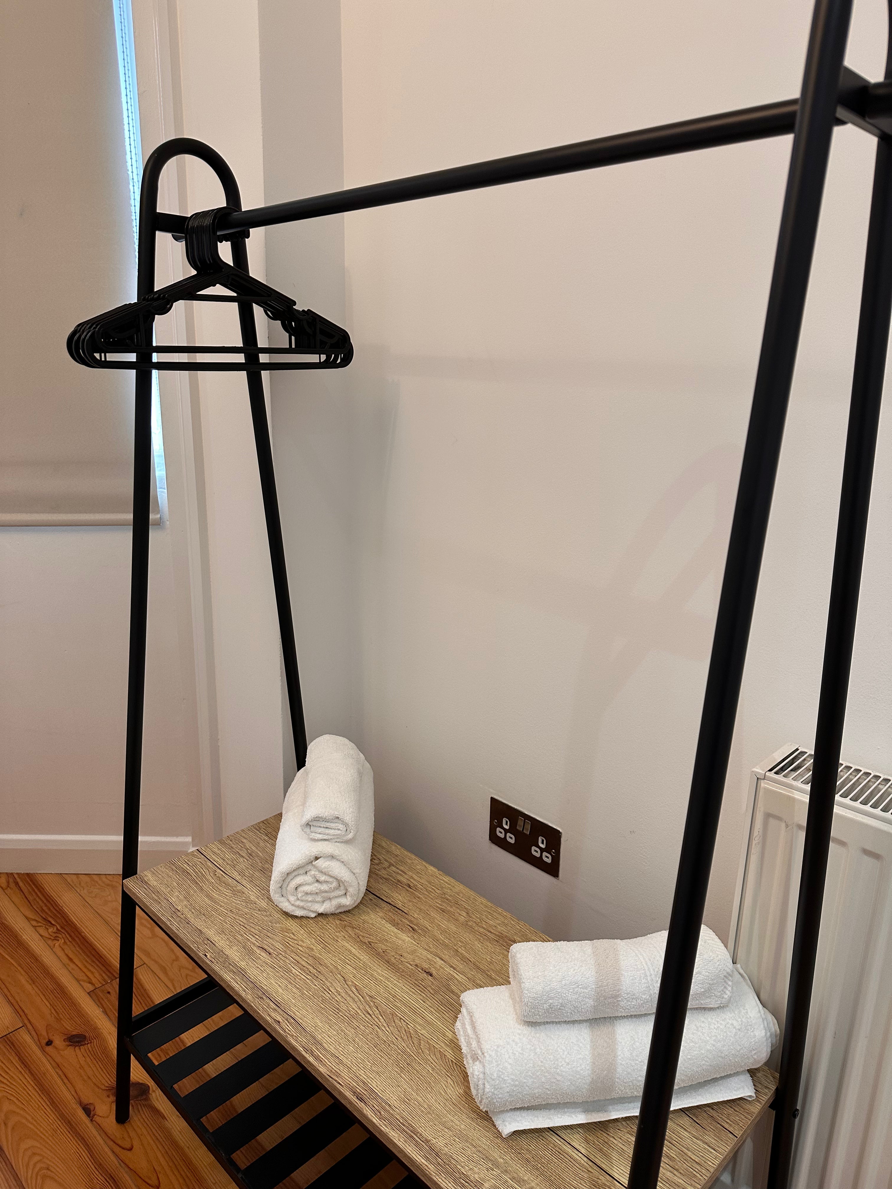 Black metal clothing rack with folded towels on a wooden platform against a white wall.