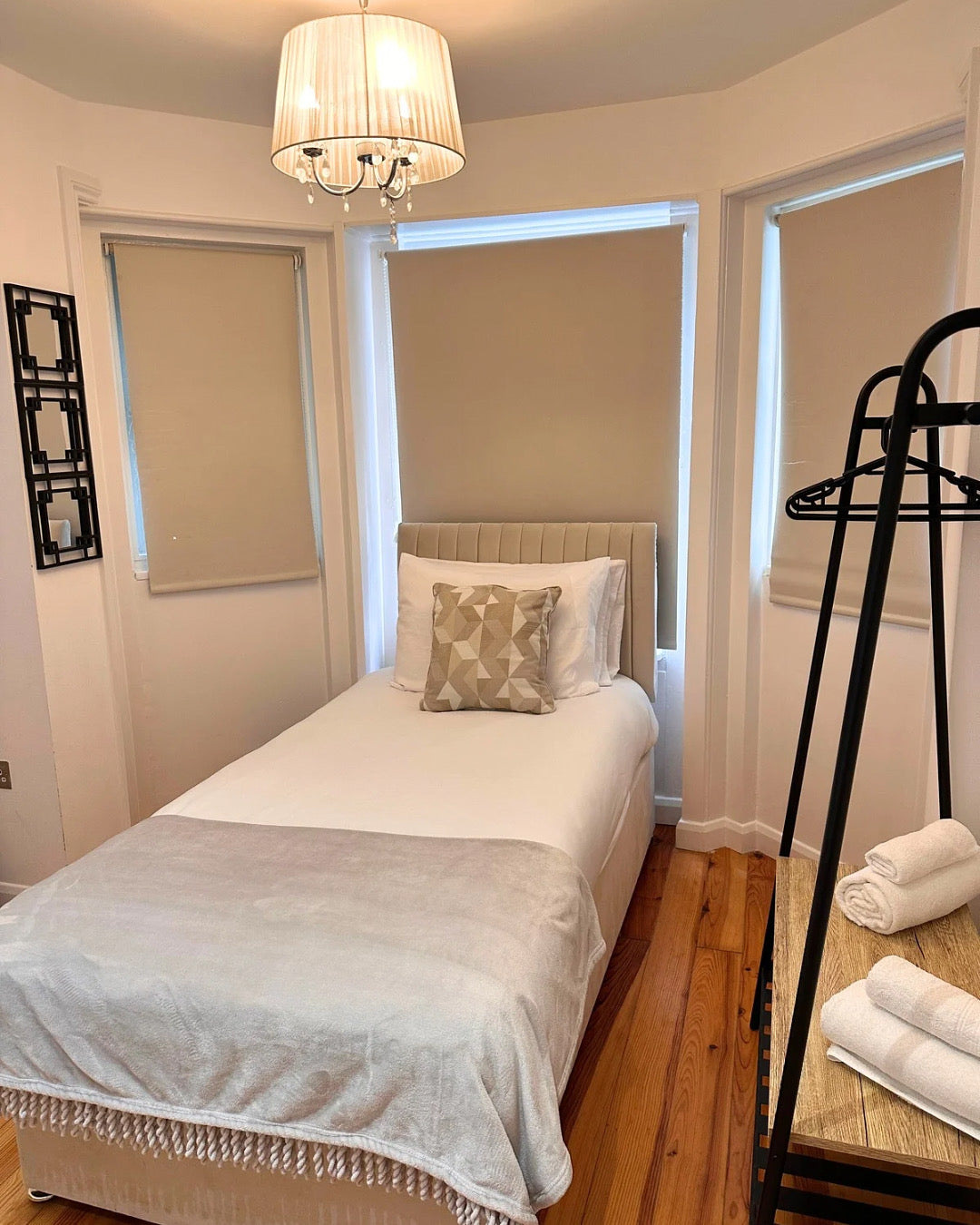 Bedroom with a single bed, wooden floor, and a stand with folded towels.